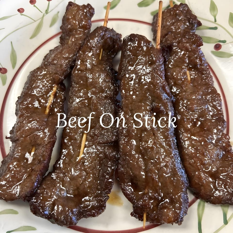 Close-up of four glistening Beef on Stick skewers from China Star, served on a white plate with a floral design.