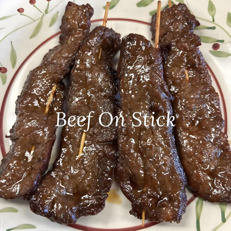 Close-up of four glistening Beef on Stick skewers from China Star, served on a white plate with a floral design.