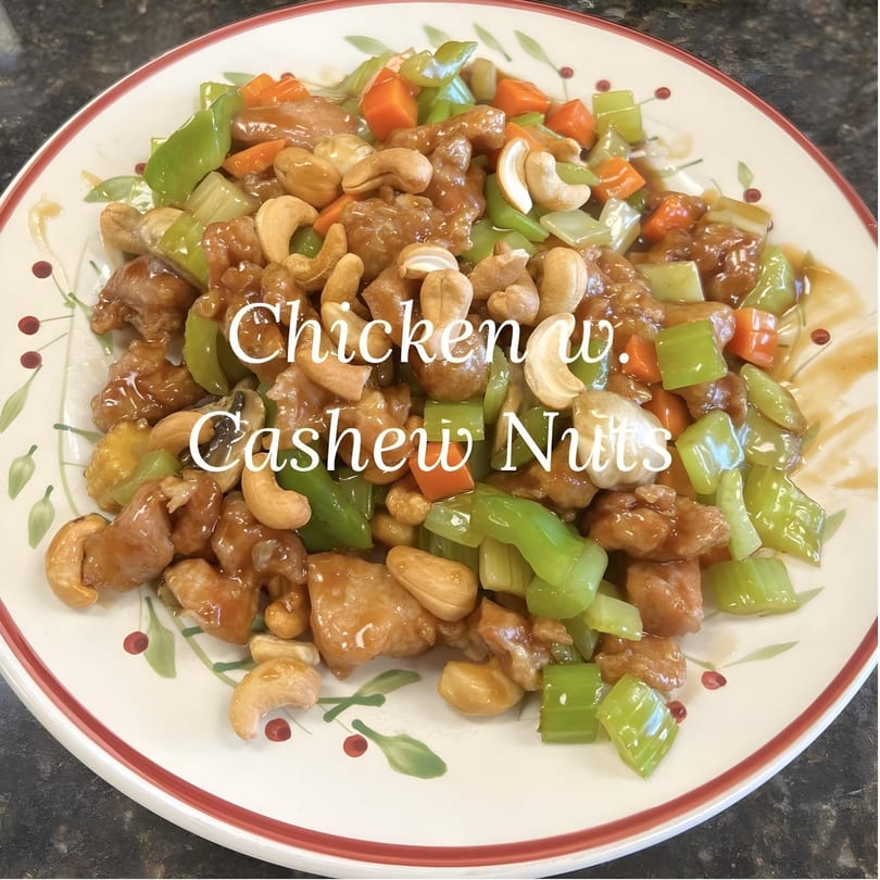 Cashew chicken with green peppers, carrots, and cashews in a brown sauce on a white plate.